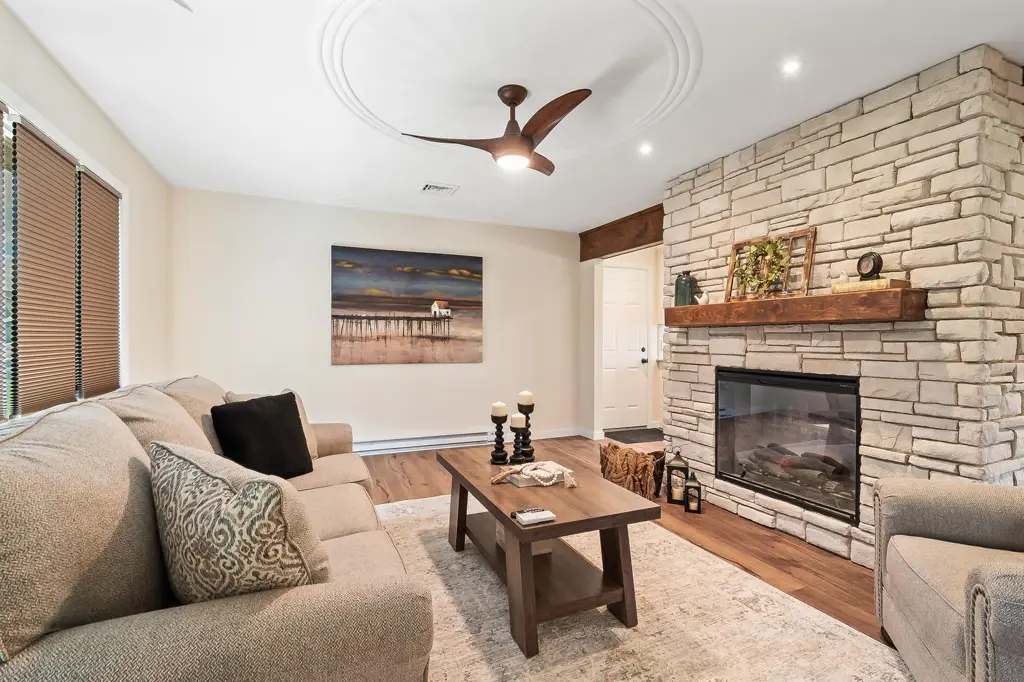 Living room with a stone fireplace, ceiling fan and sectional sofa