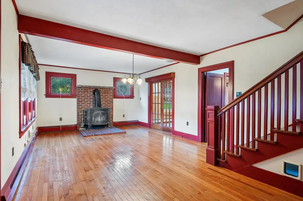 Living room with hardwood floors, a wood stove and a staircase with red trim