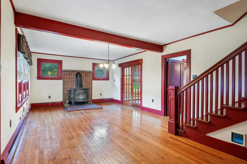 Living room with hardwood floors, a wood stove and a staircase with red trim