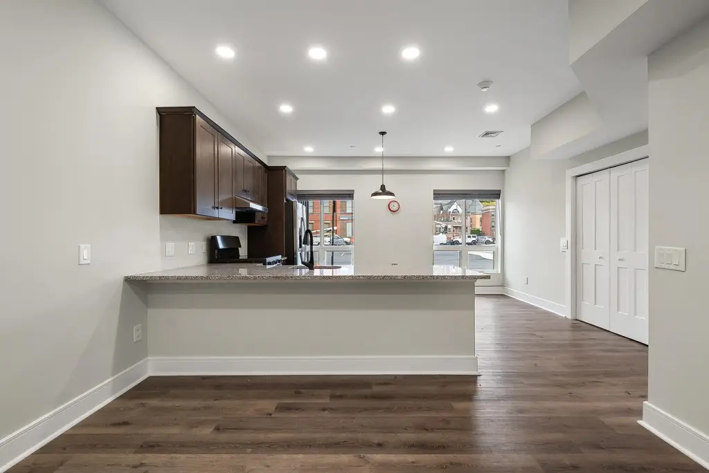 Open apartment kitchen and living area with dark cabinets and wide-plank floors